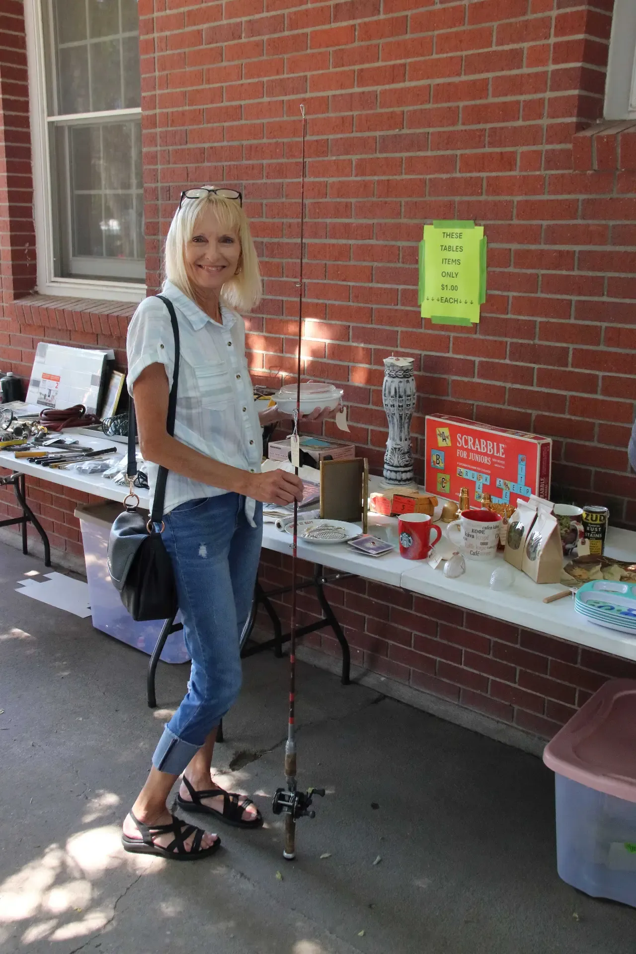 Vendor holding a fishing rod beside a table of assorted sale items