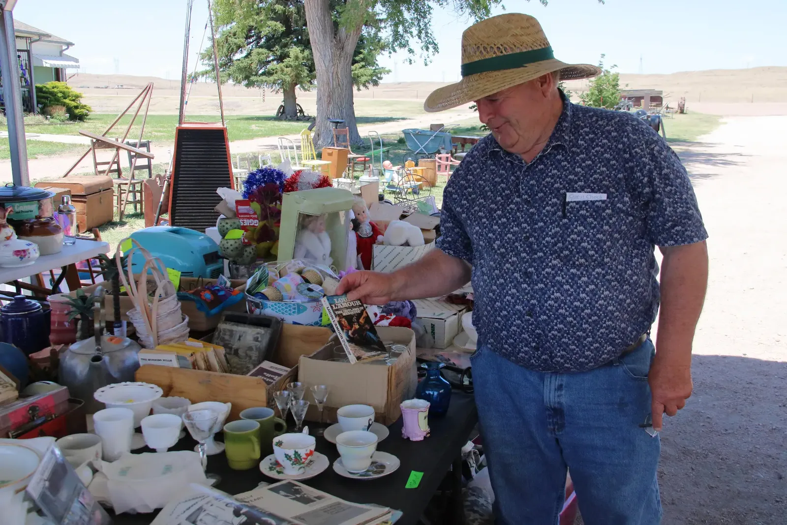 Shopper in a straw hat browsing dishes, books, and collectibles at an outdoor market table