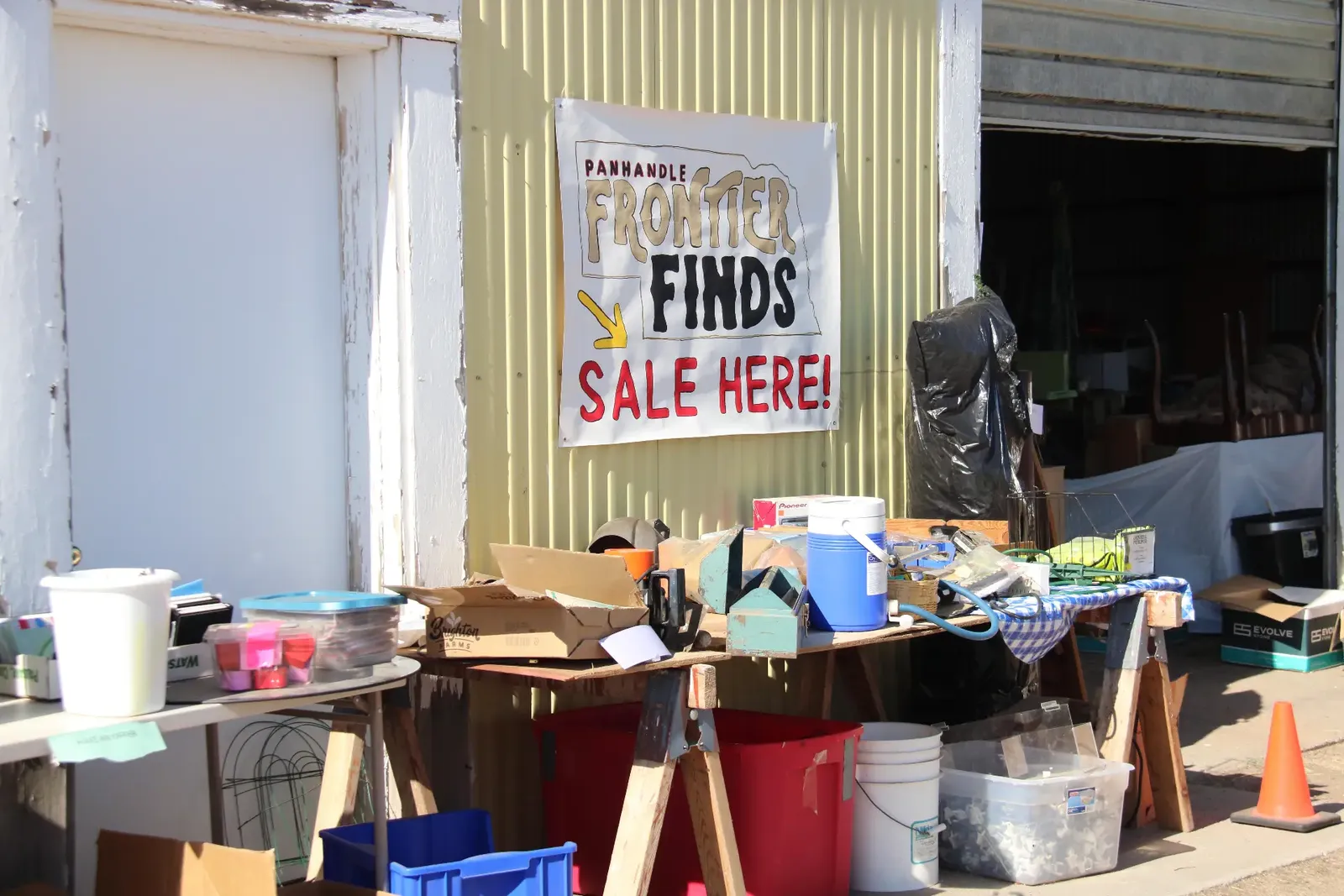 Handmade Frontier Finds sale banner hung on a barn wall above tables of assorted sale goods