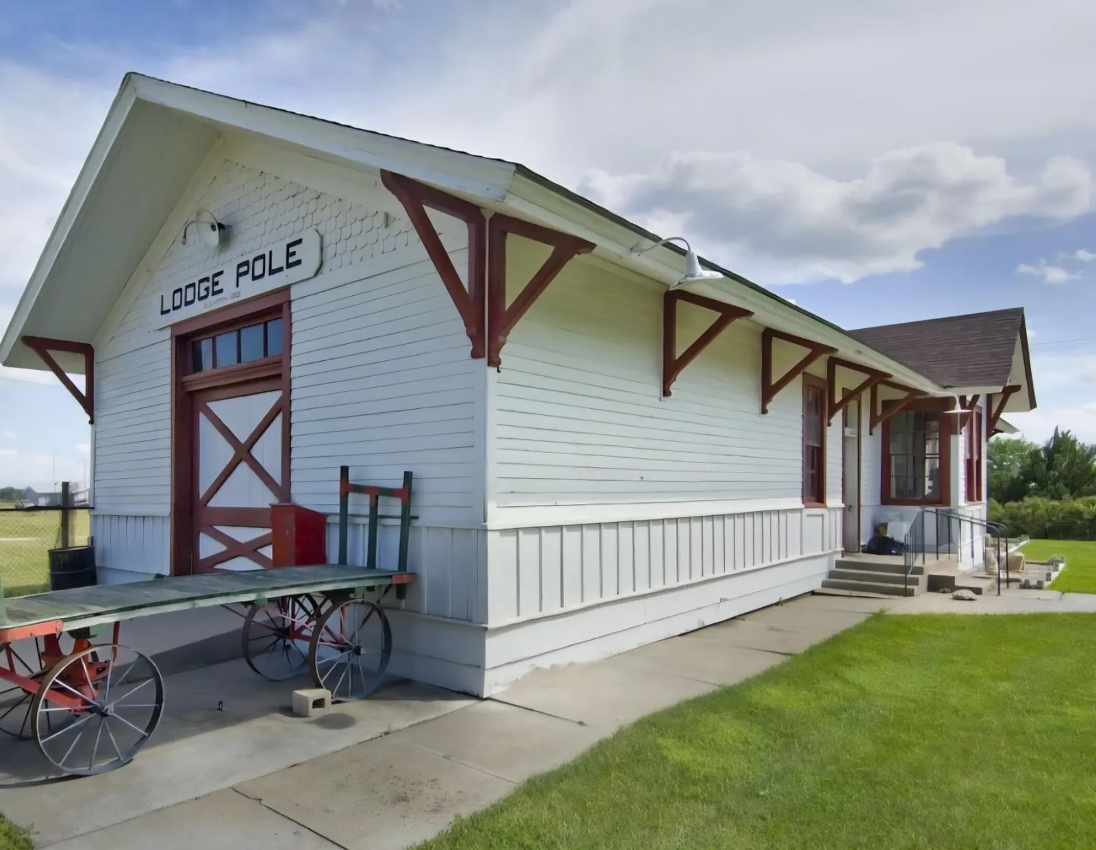Historic white Lodge Pole railroad depot with a vintage baggage cart