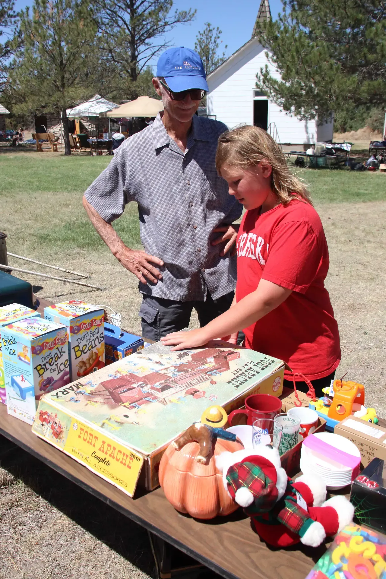 Young shopper examining a vintage Fort Apache play set box beside a vendor at an outdoor market