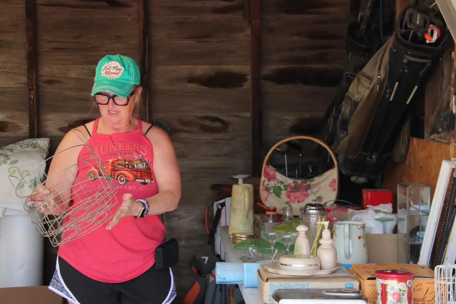 Vendor holding a wire basket beside a table of vintage household goods