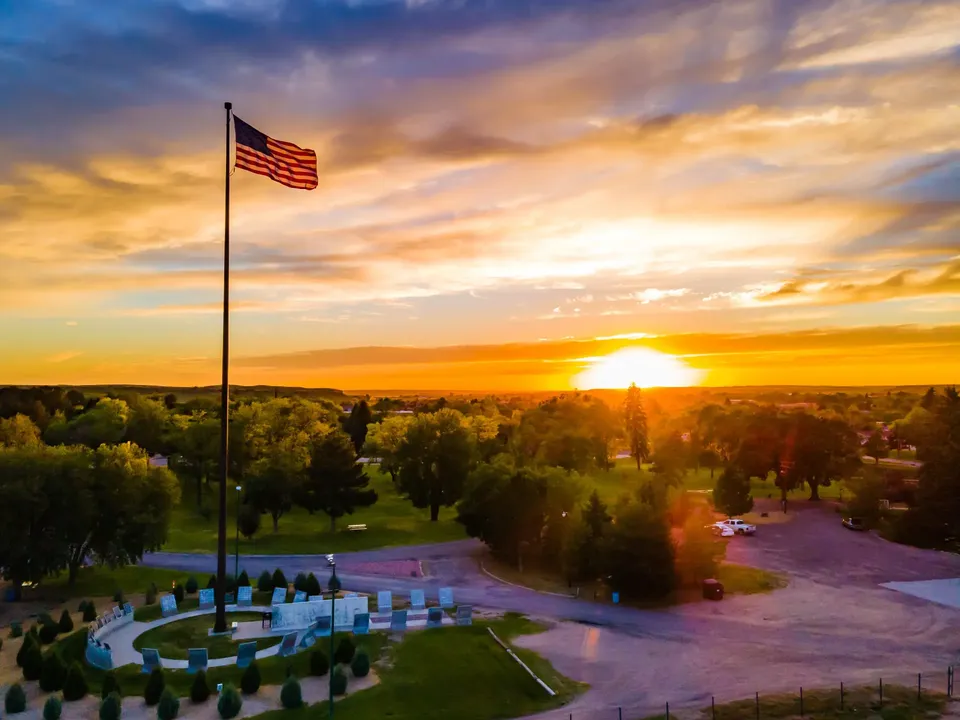 A tall American flagpole in a memorial park at sunset
